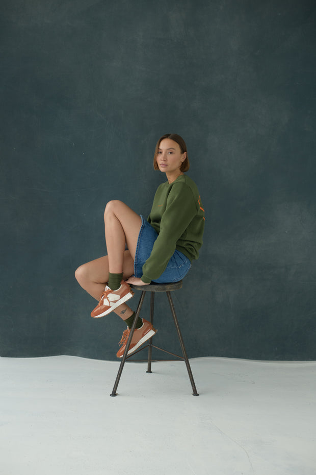 Female model wearing Urban Green & Orange Sweatshirt, sitting on a chair